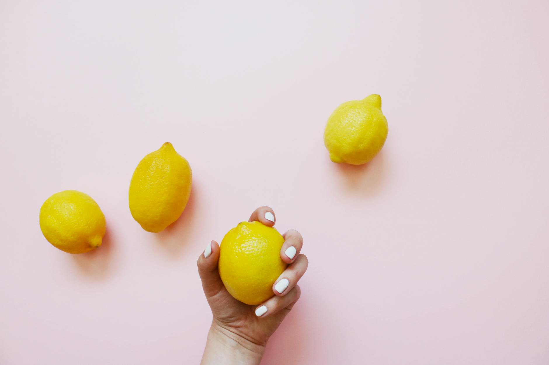 A hand holding a bright lemon on a soft pink background, symbolizing gentle, natural recovery