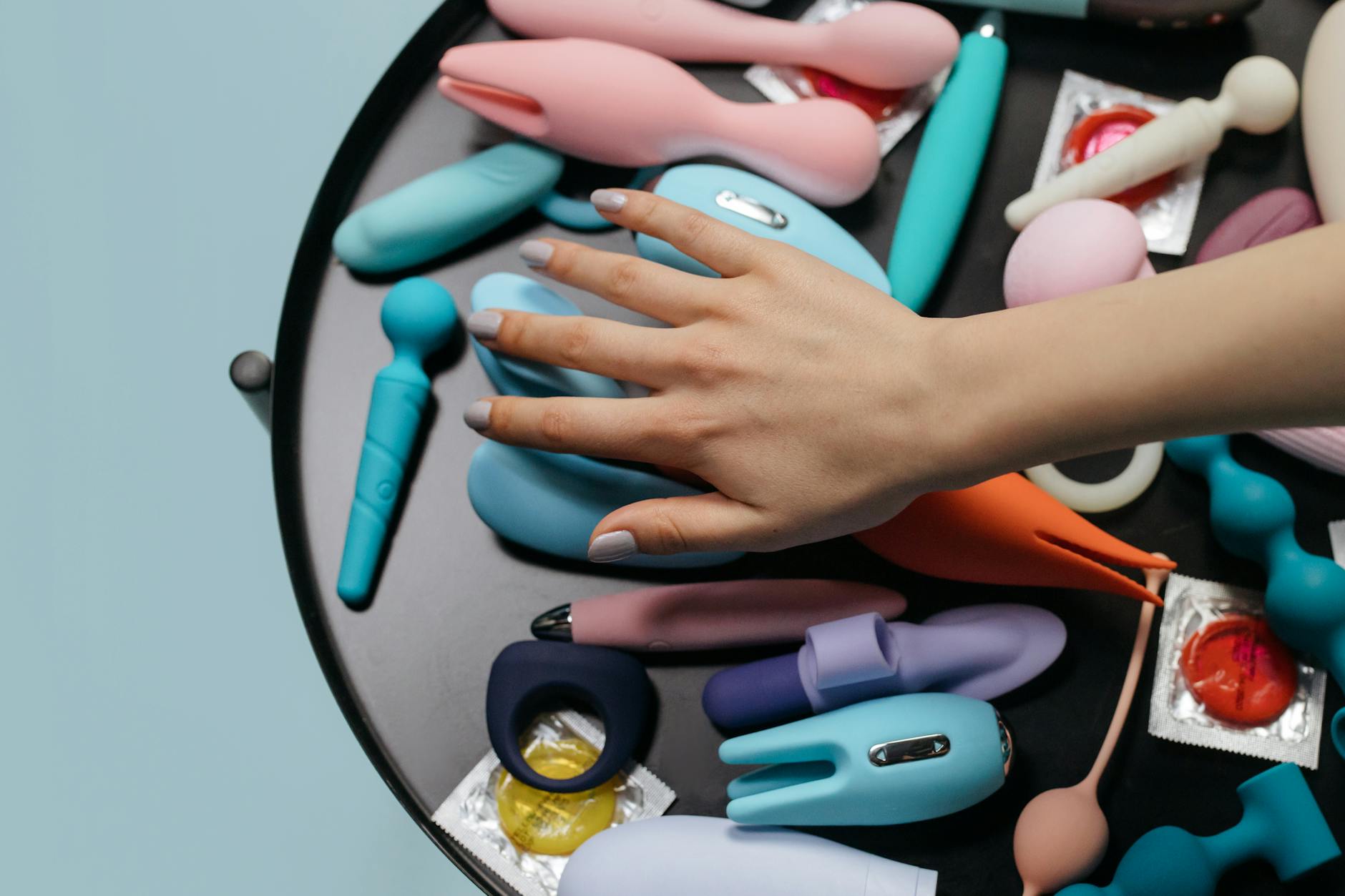 A hand holding a vibrant orange clitoral vibrator against a minimalist purple backdrop