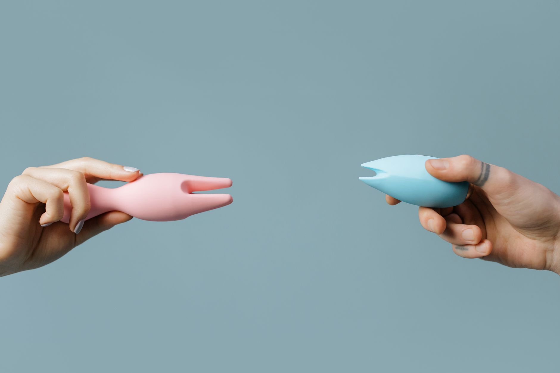 Two hands holding pink and blue silicone vibrators against a pastel background, representing different sensations throughout your cycle.