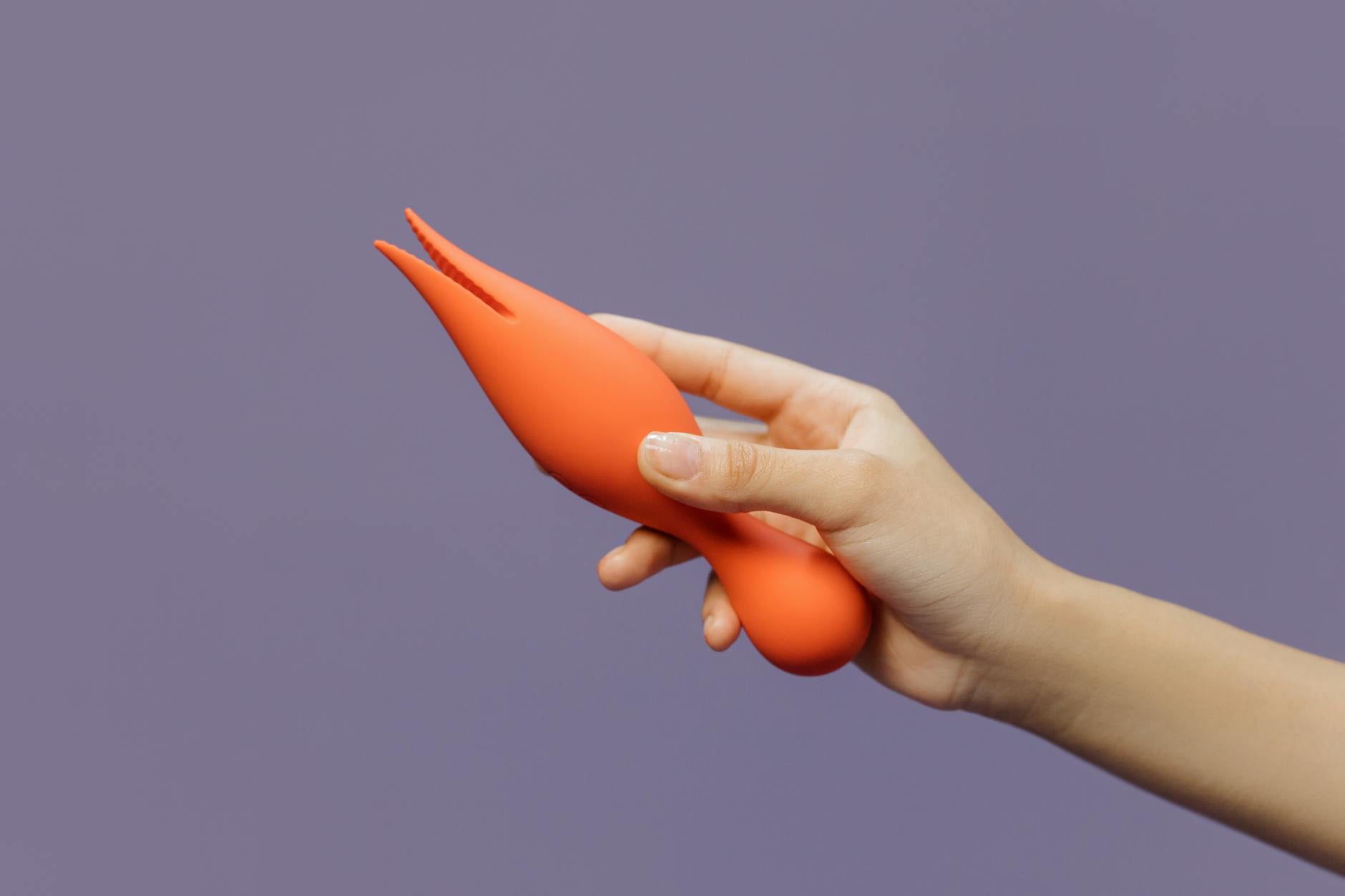 A silicone vibrator held in hand against a purple background, symbolizing self-care and shared pleasure.
