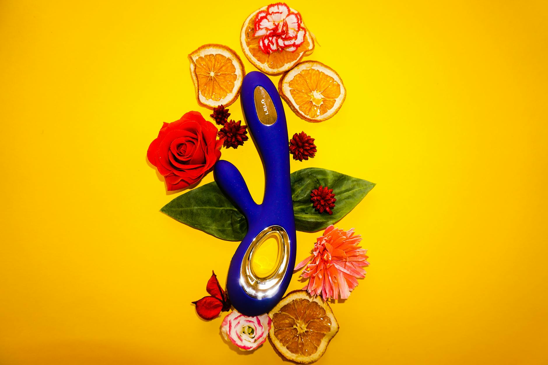 A blue vibrator surrounded by flowers and citrus slices on a bright yellow background