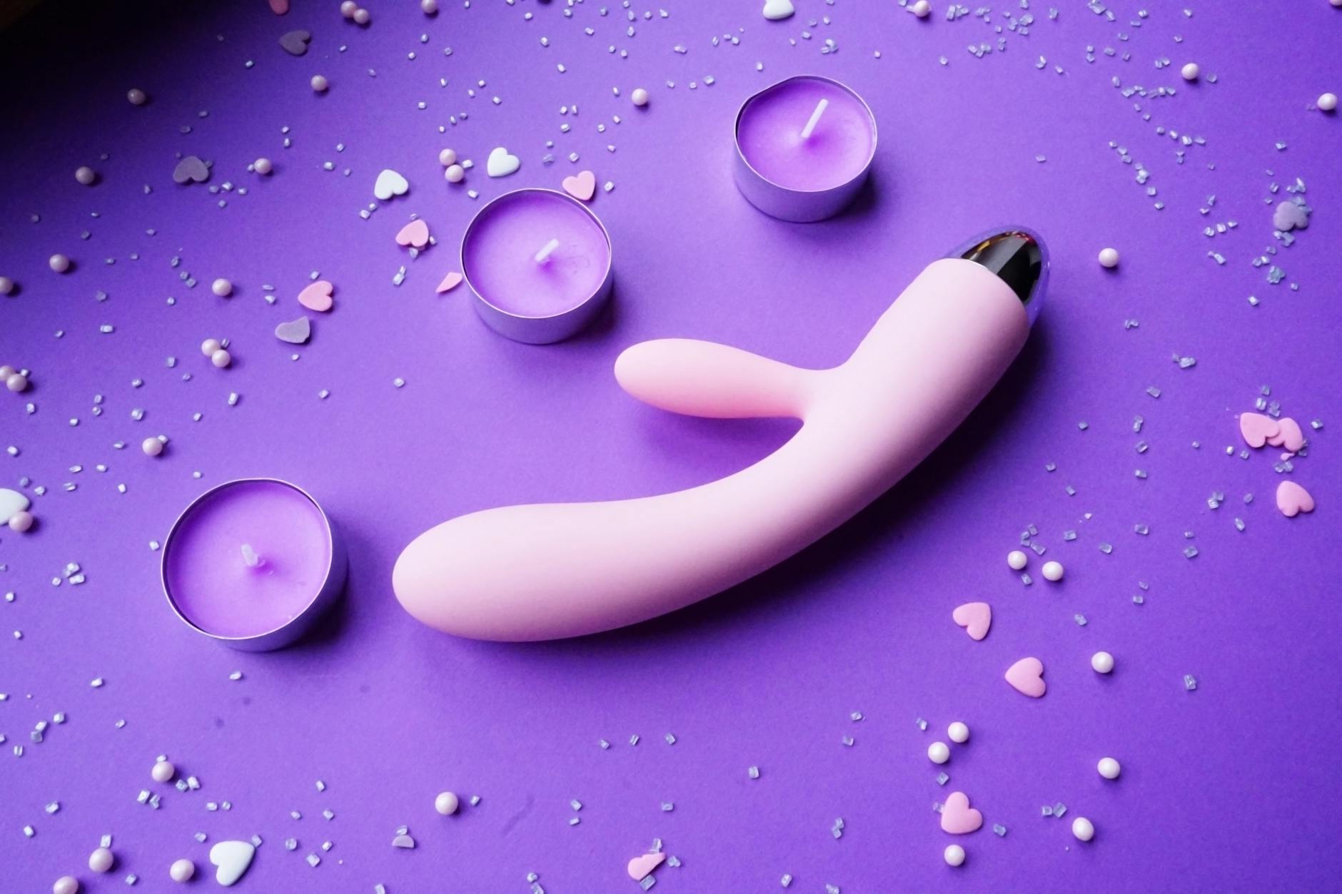 Pink vibrator on purple background with romantic candles and confetti, representing pleasure and intimacy